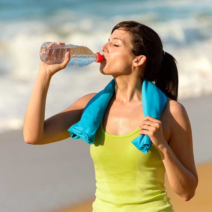 One of our weight loss trainers drinking a bottle of water during a beach walk at Weight Crafters.